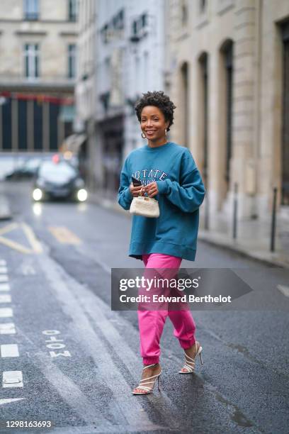 Ellie Delphine aka SlipIntoStyle wears earrings, a blue oversized wool pullover from Rotate, neon pink jogger sport pants from Rotate, a small white...