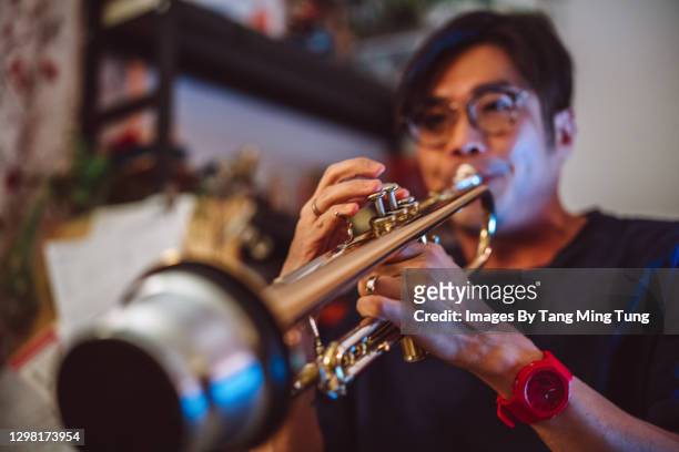 handsome asian man practising trumpet at home - guy loving music jazz stock-fotos und bilder