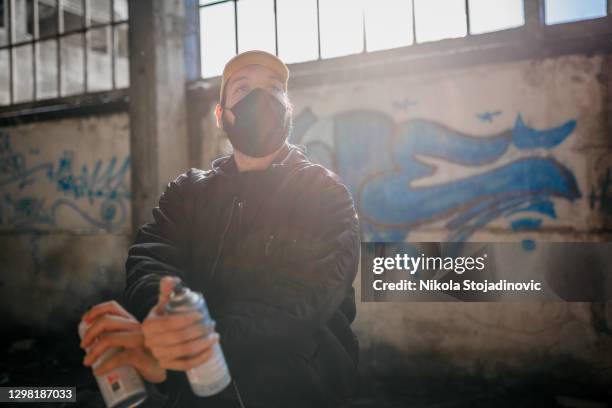 portrait of young adult graffiti artist with spray cans - thug stock pictures, royalty-free photos & images