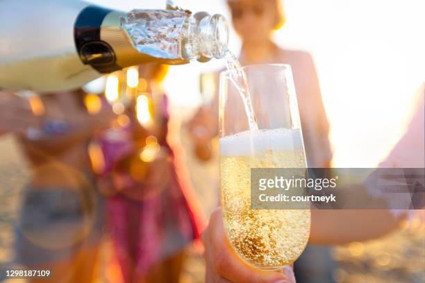 pouring a glass of champagne with people partying in the background. - champagne stock pictures, royalty-free photos & images