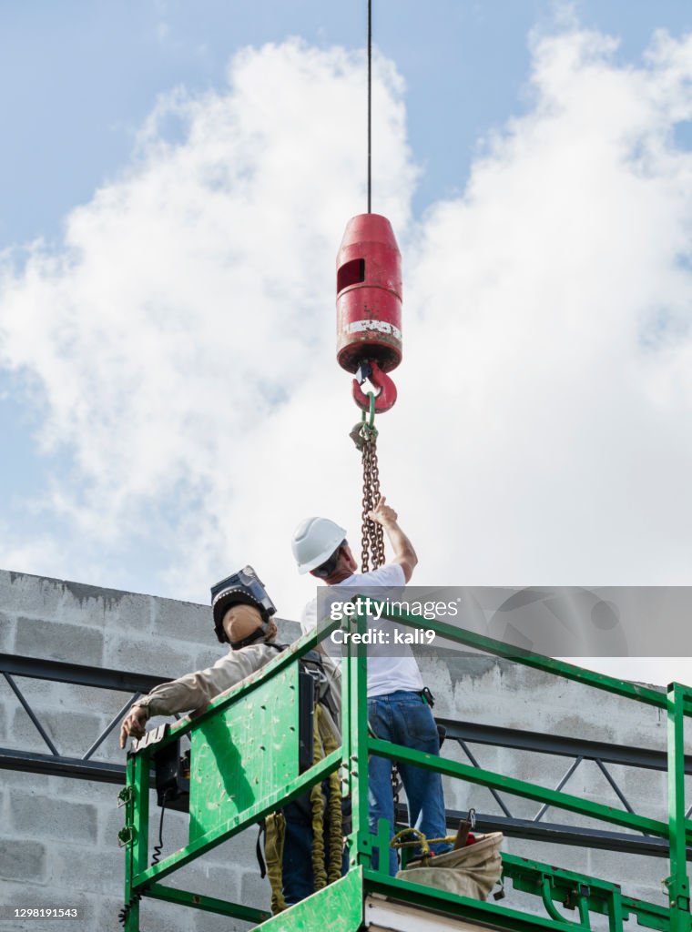Construction workers on scissor lift, with crane hook