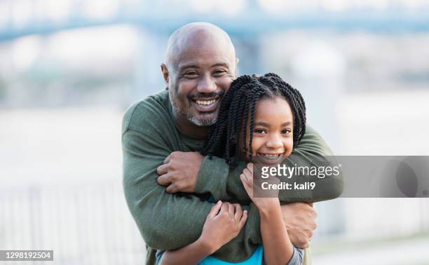 loving father embracing daughter on city waterfront - african girl hug stock pictures, royalty-free photos & images
