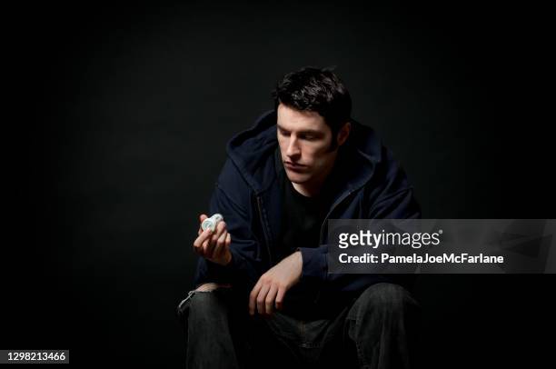 depressiver junger mann mit blick auf flasche verschreibungspflichtige medikamente - prozac stock-fotos und bilder