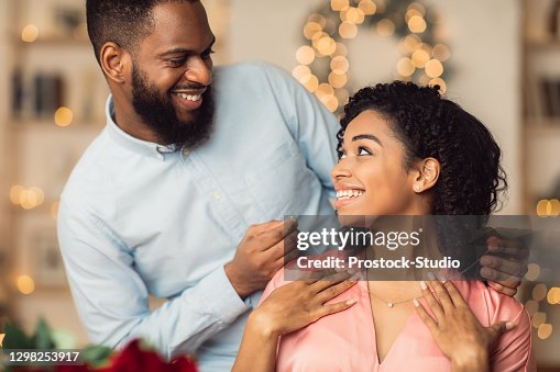 Young black guy wearing necklace on his smiling woman Young black guy wearing necklace on his smiling woman