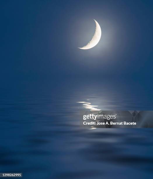 full frame of the twilight sky at sunset with the waning moon reflected on a water surface. - crescent stock pictures, royalty-free photos & images