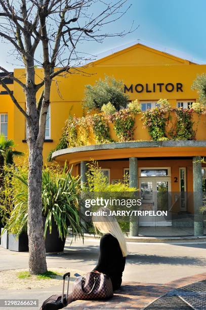 Une jeune femme blonde habillée de noir est assise sur un muret devant l'entrée de l'hôtel de Molitor et consulte son smartphone, 22 mars 2019, Paris...