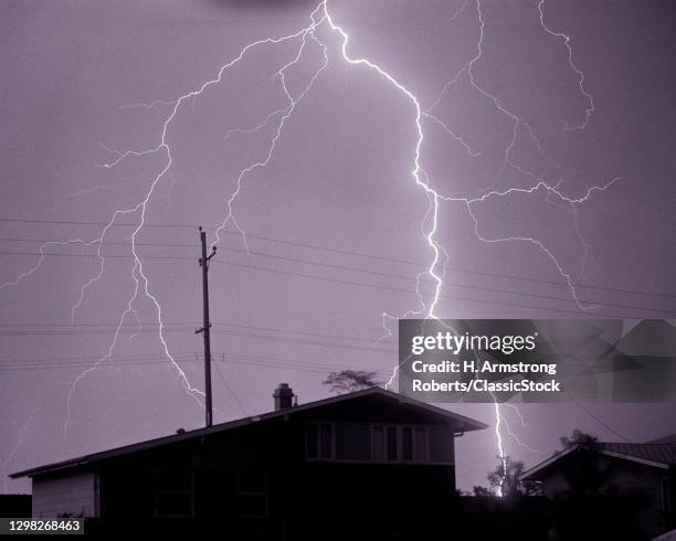 1960s Single Lightning Bolt Discharge In Sky Over Dark Residential Suburban Neighborhood Home During Night Electrical Rain Storm.