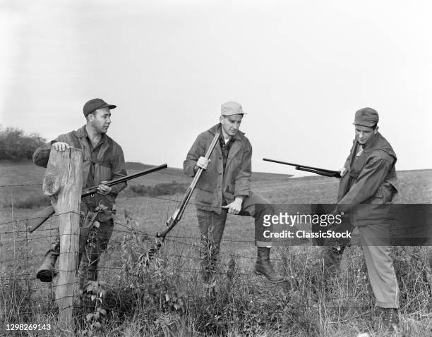 1950s 1960s Hunting Safety What Not To Do Three Men Hunters Posed In Dangerous And Unsafe Manner Climbing A Fence In The Field.