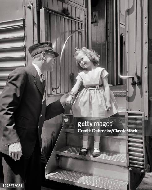 1950s Man Passenger Railroad Conductor In Uniform Greeting Smiling Little Girl Wearing Dress And Mary Jane Shores On Train Steps.