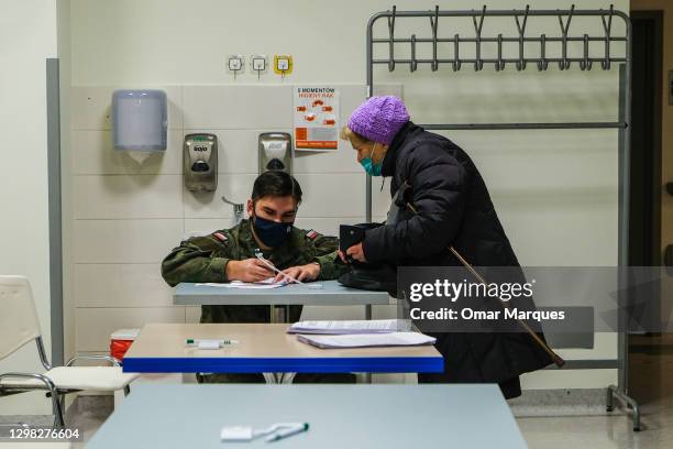 Military wears a protective face mask and gloves as helps an elderly woman to fill paperwork before the taking the Pfizer/BioNTech COVID-19 jab at...