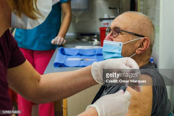 Health worker wears a protective face mask and gloves as she gives a Pfizer/BioNTech COVID-19 jab to an elderly man at the Krakow University Hospital...