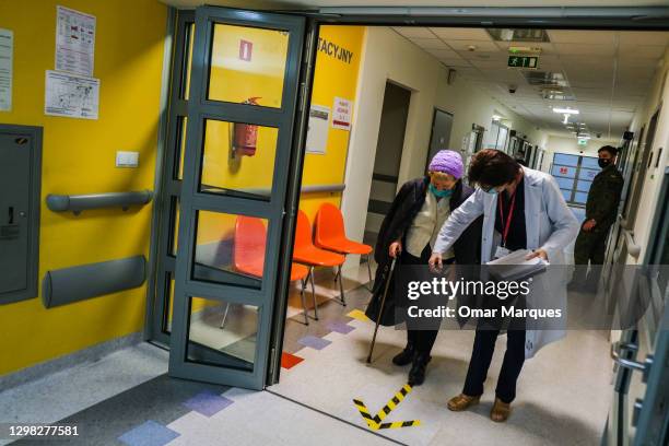 Health worker wears a protective face mask and gloves as she helps an elderly man to reach a room where he will given a Pfizer/BioNTech COVID-19 jab...