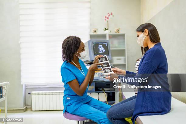 female doctor explaining ultrasound photos to a pregnant woman - prenatal care stock pictures, royalty-free photos & images