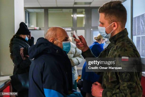 Military wears a protective face mask and gloves as he sreams the temperature of an elderly man before being given the Pfizer/BioNTech COVID-19 jab...