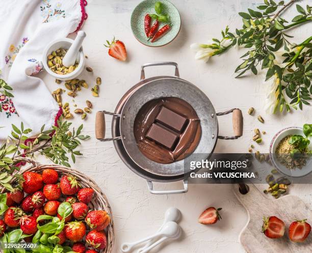 pot with melted chocolate on white kitchen table with strawberries and others tasty ingredients. - melting pot foto e immagini stock