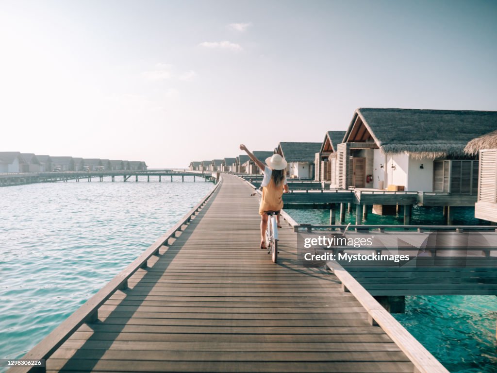Young woman riding bicycle on wooden pier in the Maldives