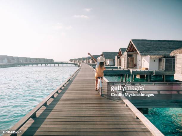 young woman riding bicycle on wooden pier in the maldives - vacations stock pictures, royalty-free photos & images