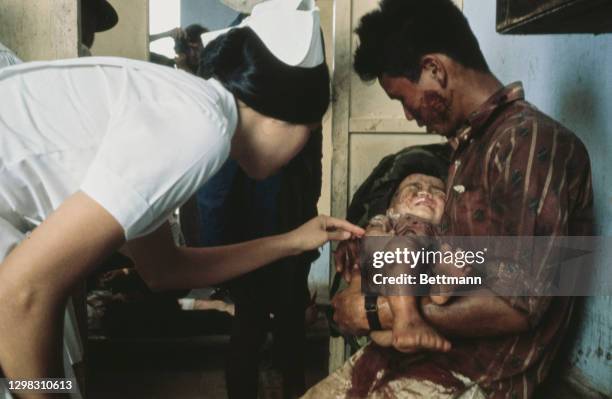 Nurse checks on a distraught Vietnamese father who holds his wounded child in his arms as both arrive for medical treatment at a hospital in Hue,...