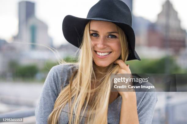 blonde female smiling with hat on and city skyline behind her - montreal people stock pictures, royalty-free photos & images