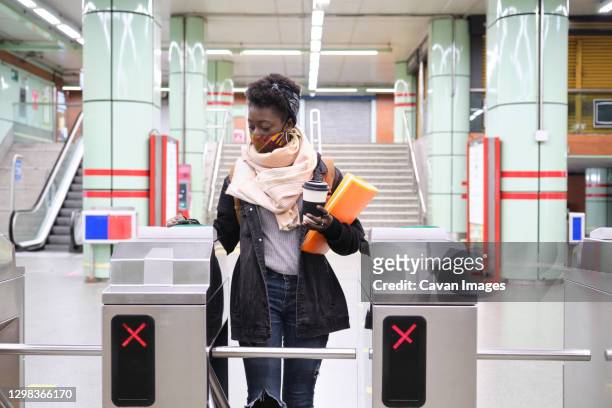 university female african student wearing protective face mask passing through the turnstiles with her transport card at the underground station. new normal in public transport. - entering turnstile stock pictures, royalty-free photos & images