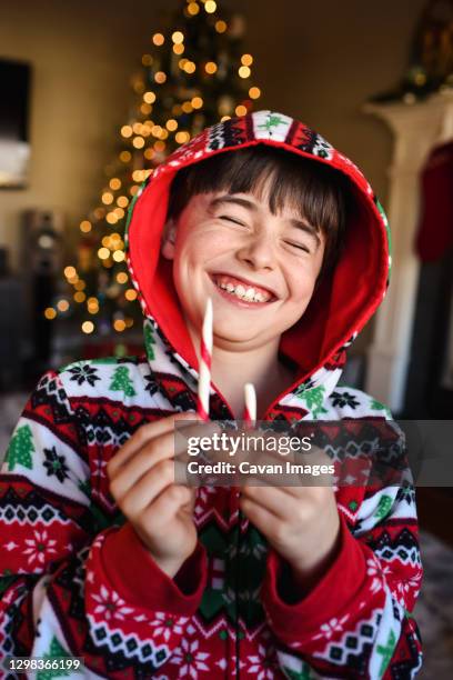 happy boy in festive pajamas eating a candy cane at christmas time. - candy cane stock pictures, royalty-free photos & images