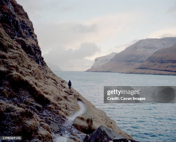 female hiker walking along cliff in the faroe islands - faroe islands stock pictures, royalty-free photos & images