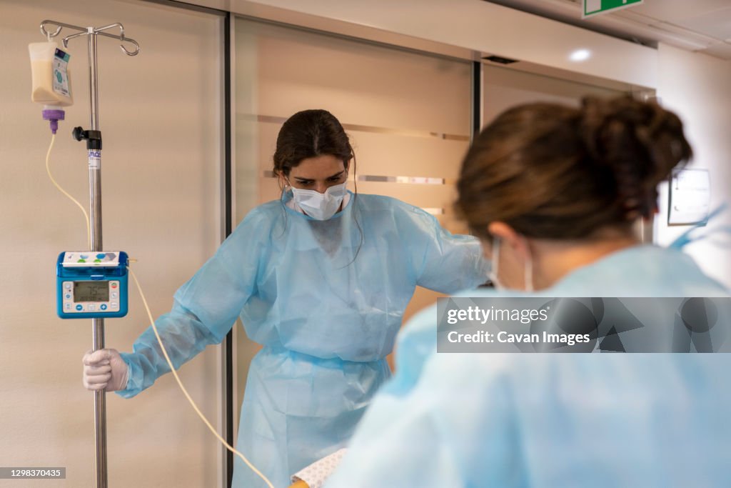 Two nurses help a patient walk in a hallway