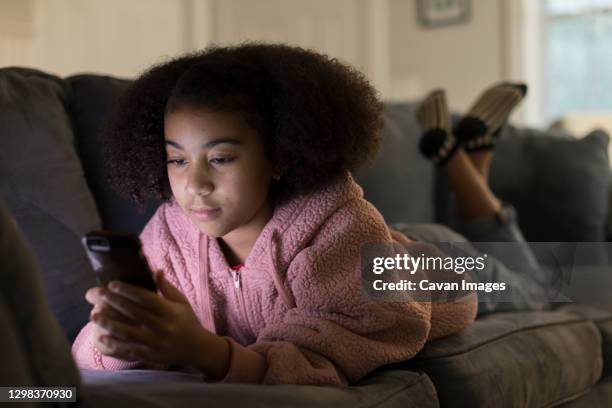 ten year-old bi-racial girl looking at her cell phone while l - 13 year old black girl stockfoto's en -beelden