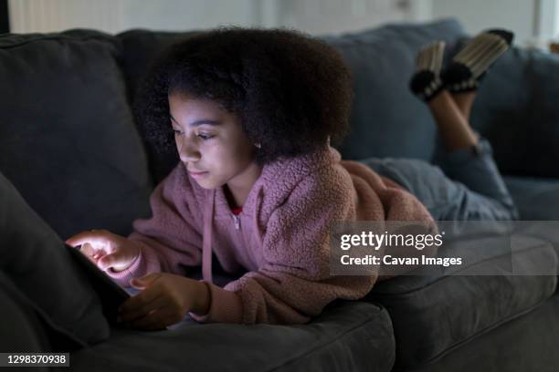 ten year-old bi-racial girl working on her tablet computer while lying on sofa - 13 year old black girl stock-fotos und bilder