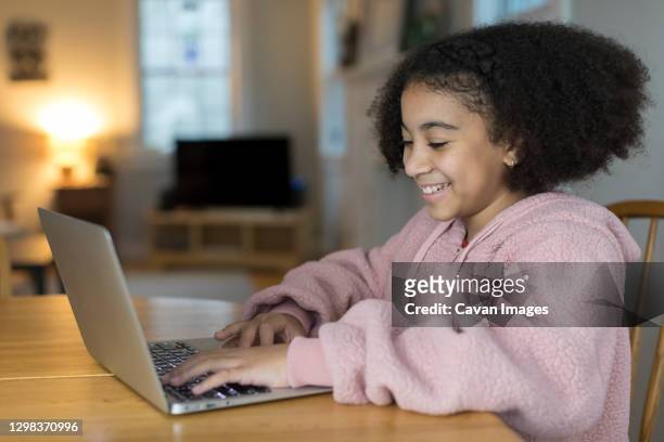 smiling ten year-old bi-racial girl working on laptop at table - 13 year old black girl stock-fotos und bilder