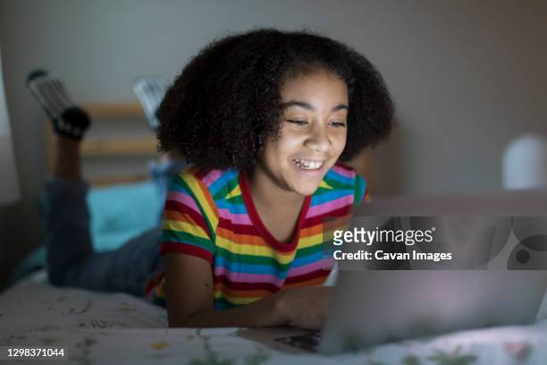 smiling ten year-old bi-racial girl working on her apple laptop on bed - 13 year old black girl stockfoto's en -beelden