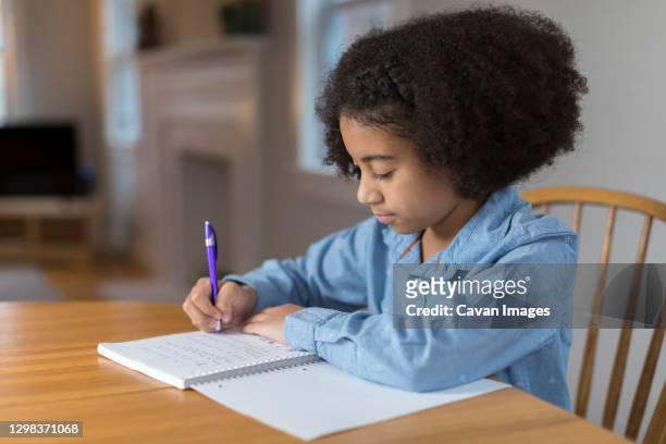 ten year-old bi-racial girl doing homework at table - 13 year old black girl stockfoto's en -beelden