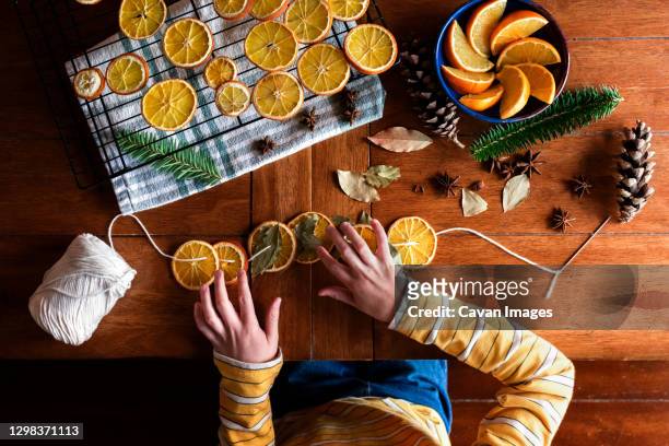 childs hands putting together dried orange garland for christmas - craft food fotografías e imágenes de stock