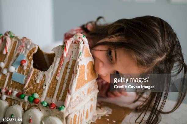 young female child eating gingerbread house big bite - gingerbread house stockfoto's en -beelden