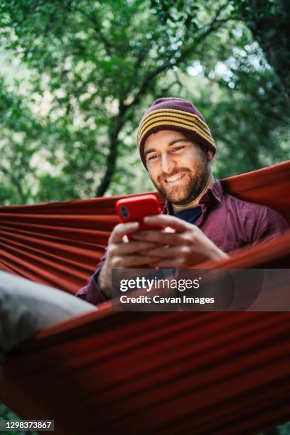 young male uses his smartphone resting on a hammock in the woods - smartphones dangling stock pictures, royalty-free photos & images