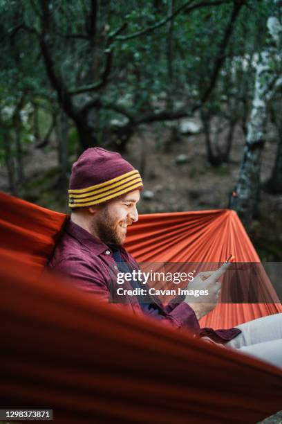 young male uses his smartphone resting on a hammock in the woods - smartphones dangling stock pictures, royalty-free photos & images