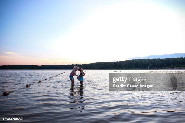 two girls playing in water on a lake at sunset in summertime - brandloch stockfoto's en -beelden