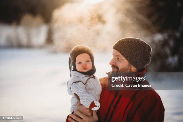 dad and beautiful baby outside in snow in winter during golden sunset - baby winter farm son stock pictures, royalty-free photos & images