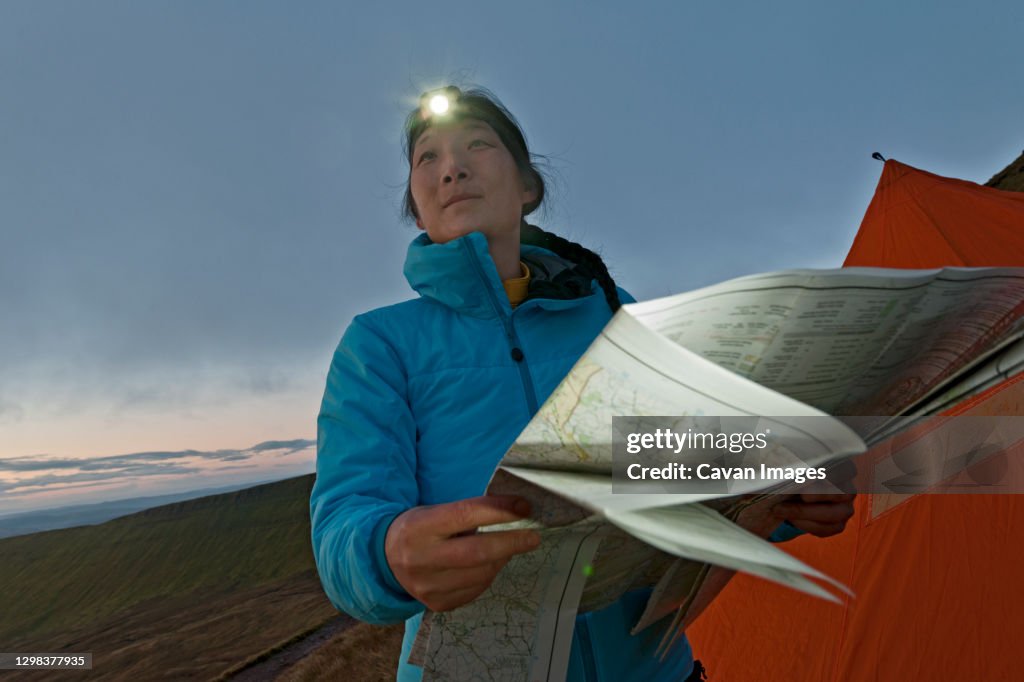 Female hiker reading hiking map on Pen Y Fan in Wales at sunrise