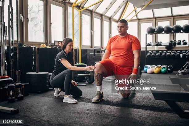 entrenadora personal femenina que muestra a su aprendiz masculina la manera correcta de hacer ejercicio - hombre sobrepeso fotografías e imágenes de stock
