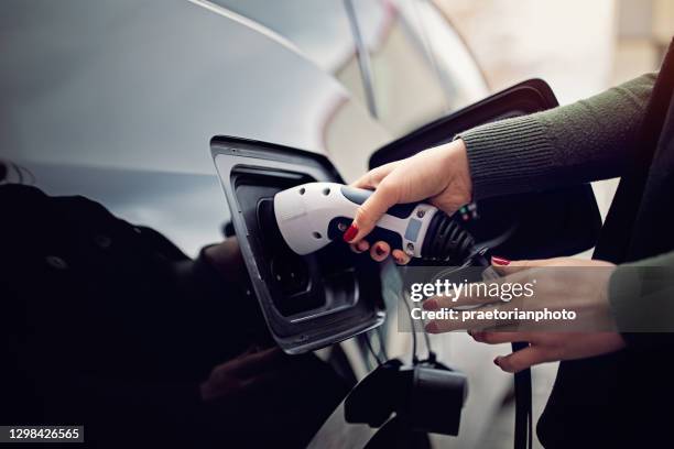 woman is plugging/unplugging cable to electric car - hybrid car charging stock pictures, royalty-free photos & images