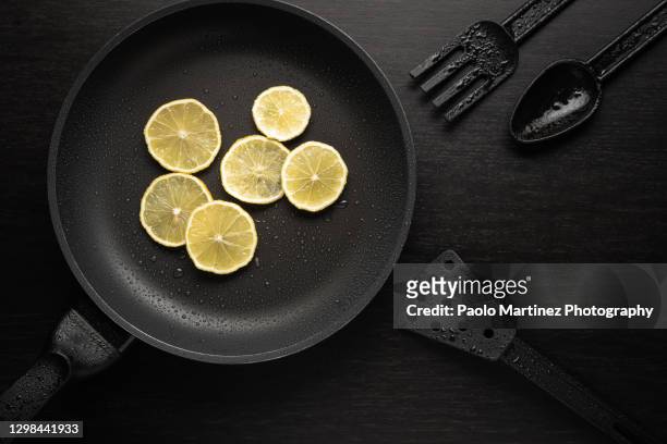 lemon slices onto black frying pan with a non-stick teflon coating on black background - polytetrafluoroethylene stock pictures, royalty-free photos & images