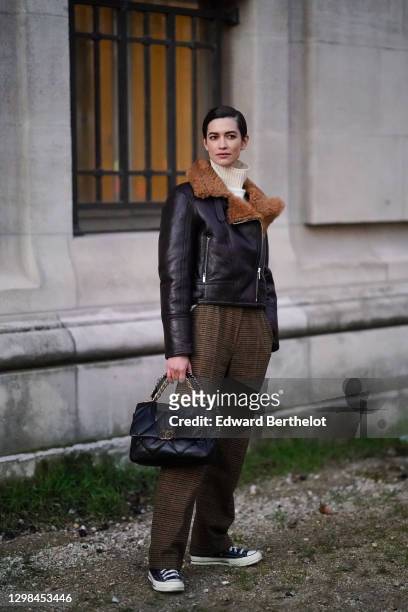 Model Louise de Chevigny wears a white wool turtleneck pullover, a brown leather aviator winter jacket with fluffy inner lining, brown suit pants...