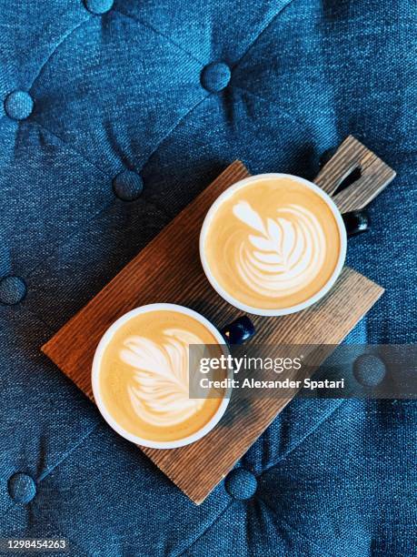 two cups of cappuccino with latte art on a wooden board, high angle view - cappuccino stock-fotos und bilder