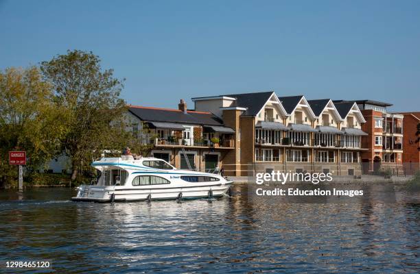 Eton, Buckinghamshire, England, UK, Cabin cruiser passing modern housing along the River Thames seen from Windsor looking to the Eton riverside.