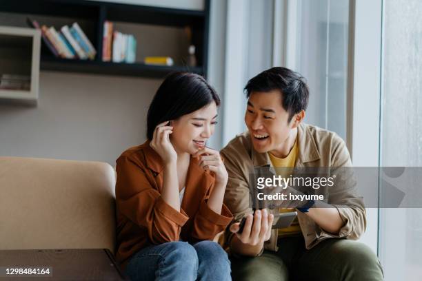 coppia cinese asiatica felice e sorridente che guarda uno spettacolo su smartphone insieme - apartment living asian foto e immagini stock