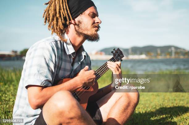 ein mann in dreadlocks spielen ukulele am rande des teiches - ukulele stock-fotos und bilder