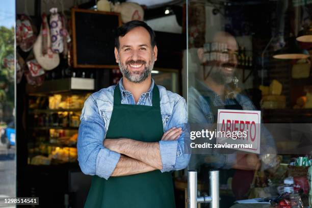 portrait of cheerful male shopkeeper standing at front door - retail store opening stock pictures, royalty-free photos & images