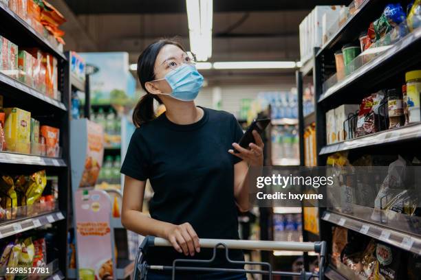 asian woman with protective face mask shopping for groceries in supermarket - asian supermarket stock pictures, royalty-free photos & images