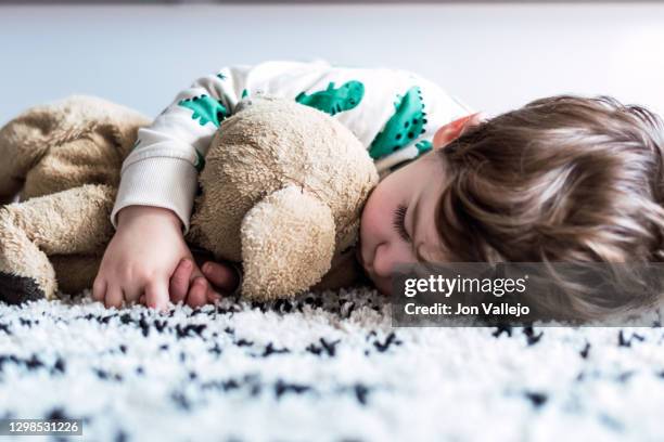 close-up of a child hugging his stuffed dog as he sleeps on top of the carpet. - chien en peluche photos et images de collection